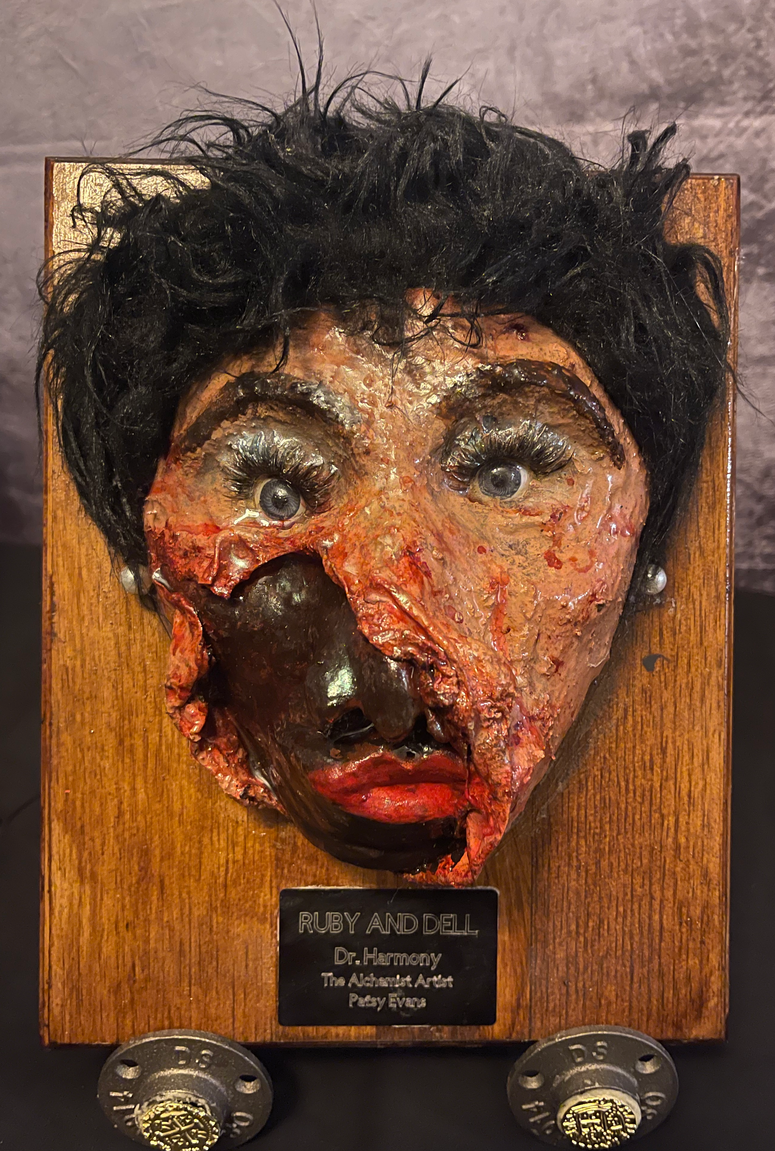 Ruby as Dell, a layered sculptural face mounted on a wooden panel